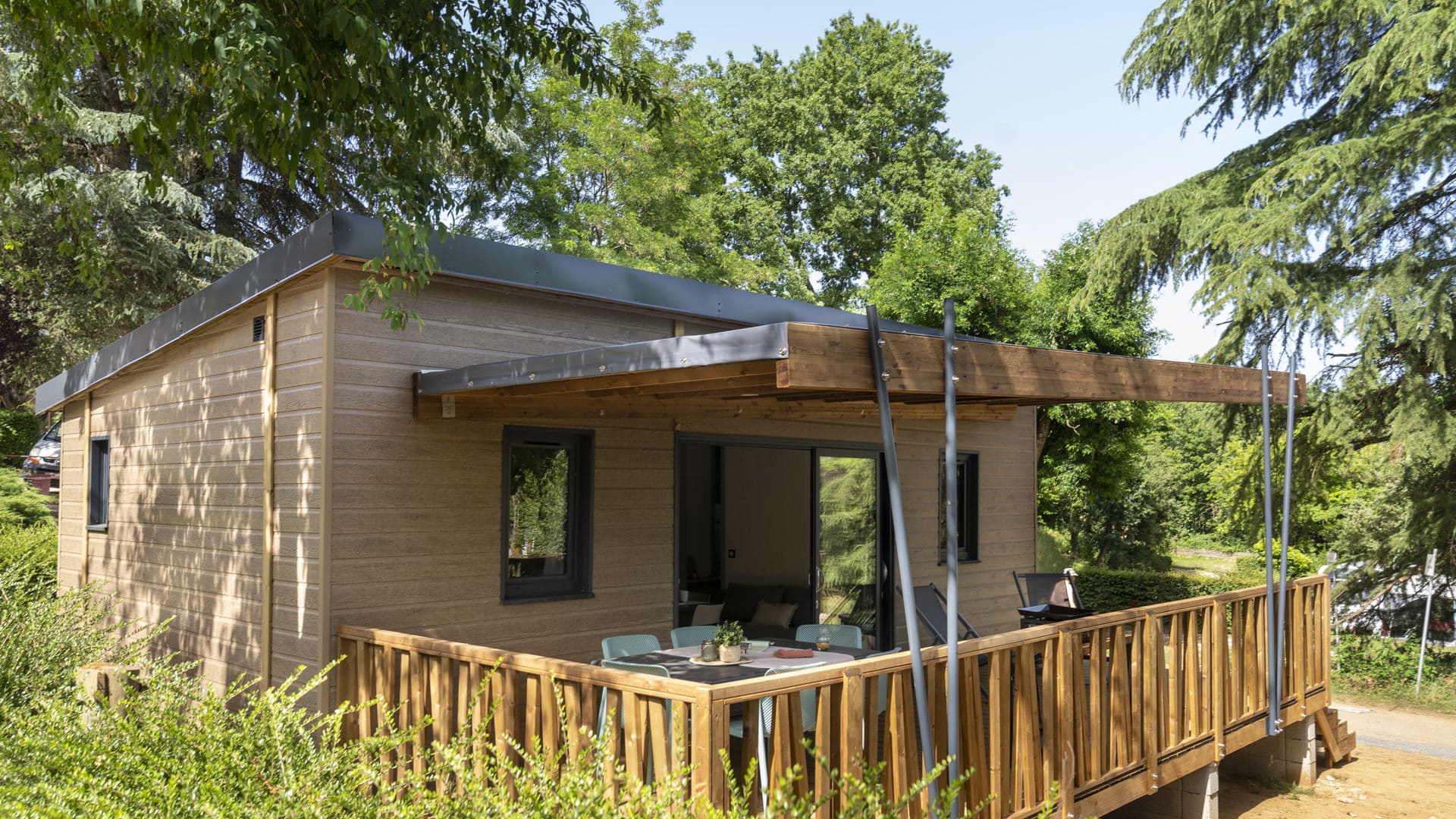 Mobil-home avec terrasse en bois, entouré d'arbres.